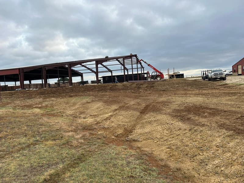 Red iron frame of an arena cover going up with a crane, seen across the graded pad