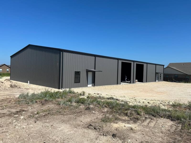 Large dark brown metal shop with two bay openings and a walk door on a gravel pad