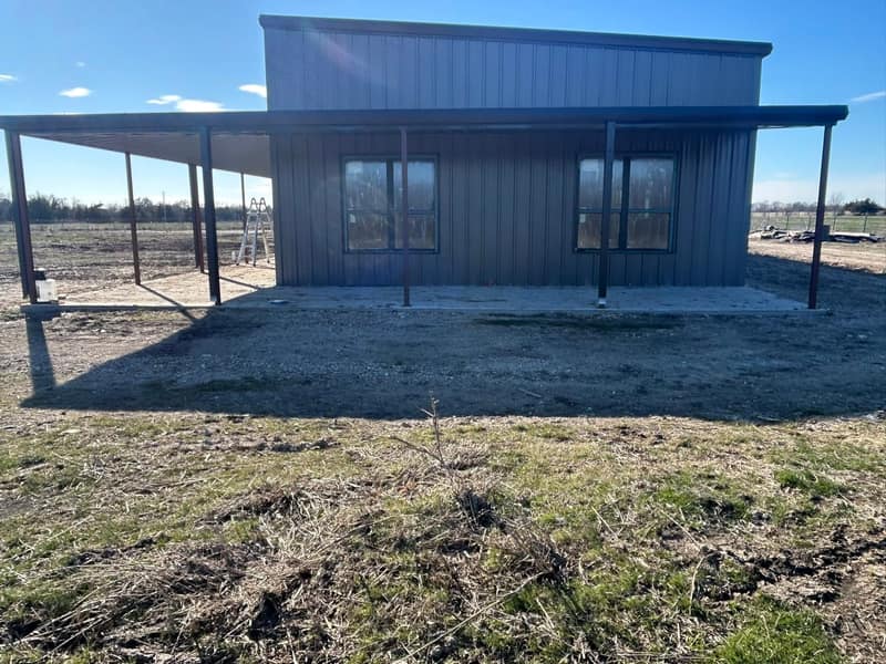Charcoal metal barndominium seen from the porch end, windows along the wall and open pasture behind