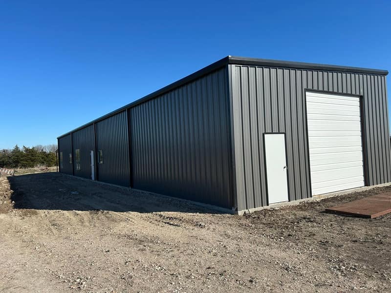 Long charcoal metal building with a white roll-up door at the end and a walk door on the side