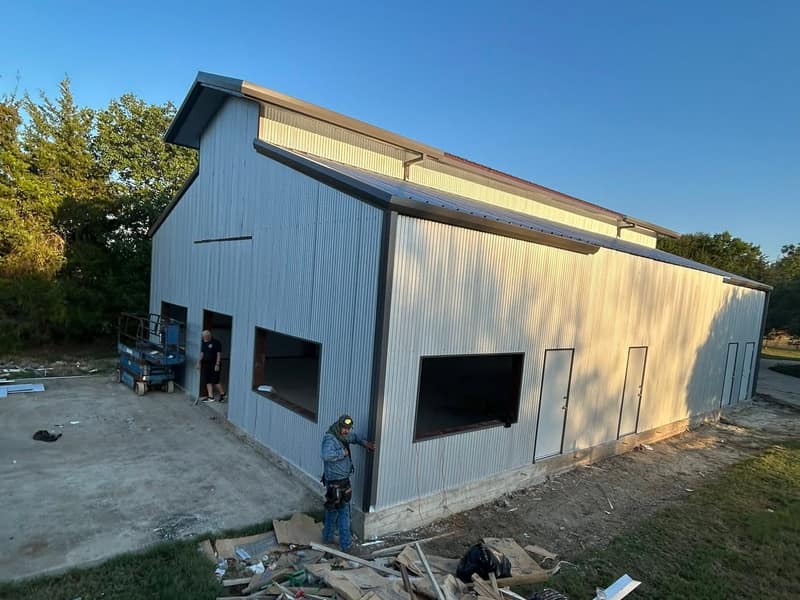 Crew on a scissor lift finishing the trim on a light gray metal shop in evening light