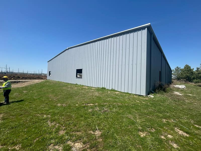 Long side wall of a tall light gray metal warehouse with a single walk door, crew member in the foreground