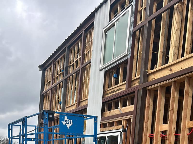 Scissor lift beside the wood-framed wall and a set window of a two-story metal barndominium