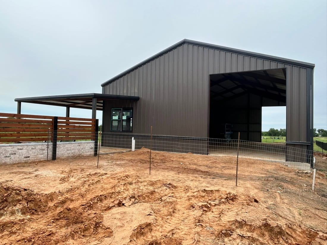 Brown metal barn with pipe fencing being set on a dirt lot