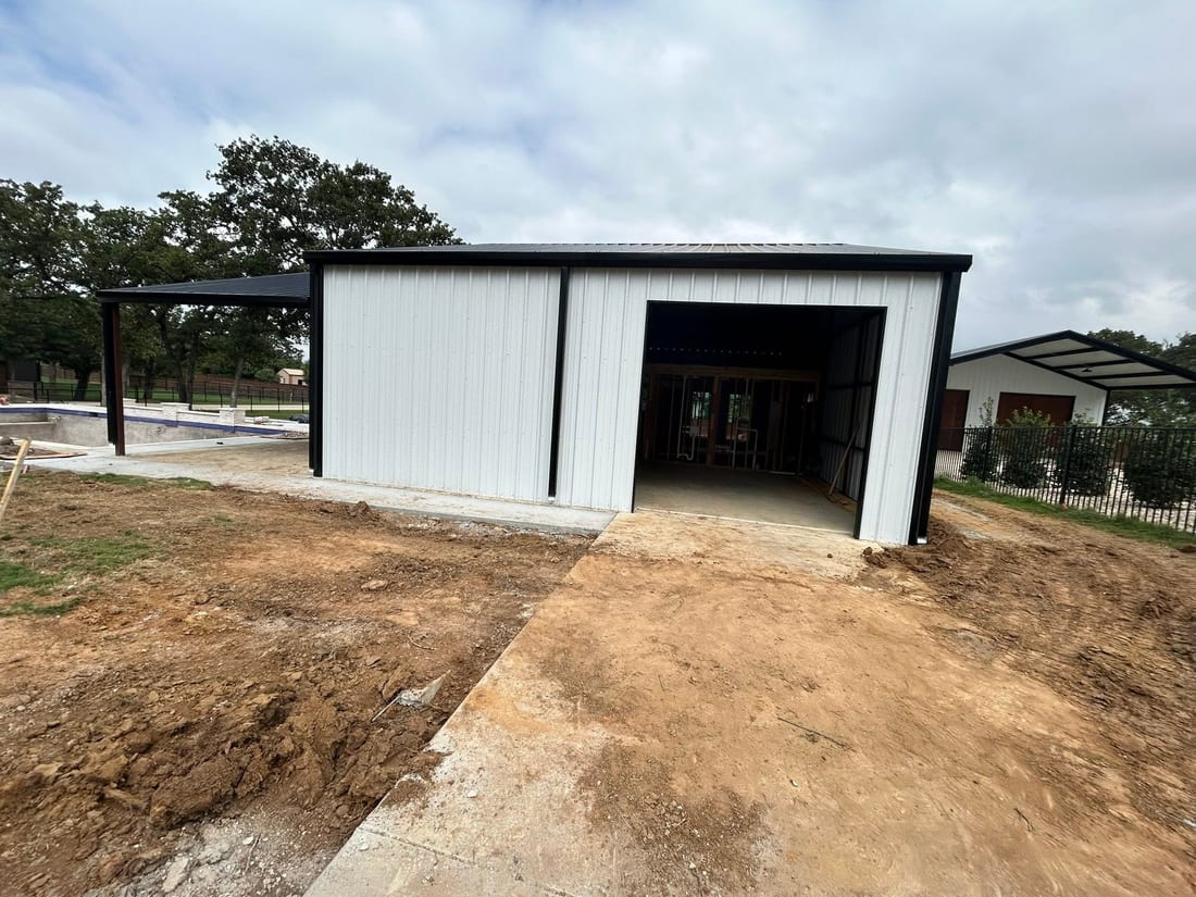 White metal shop with an open roll-up door on a fresh concrete pad